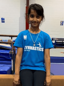 Gymnastics member with blue PCYC gymnastics shirt and black leggings sitting on balance beam