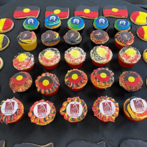 Cookies in roows with Aboriginal flag (black and red rectangles stacked with yellow circle in centre. Torres Stait flag on cupcakes, NAIDOC logo and PCYC Queensland logo. 