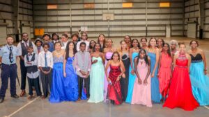 Group of people in basketball court with formal attire on. Various colours gowns and suits.