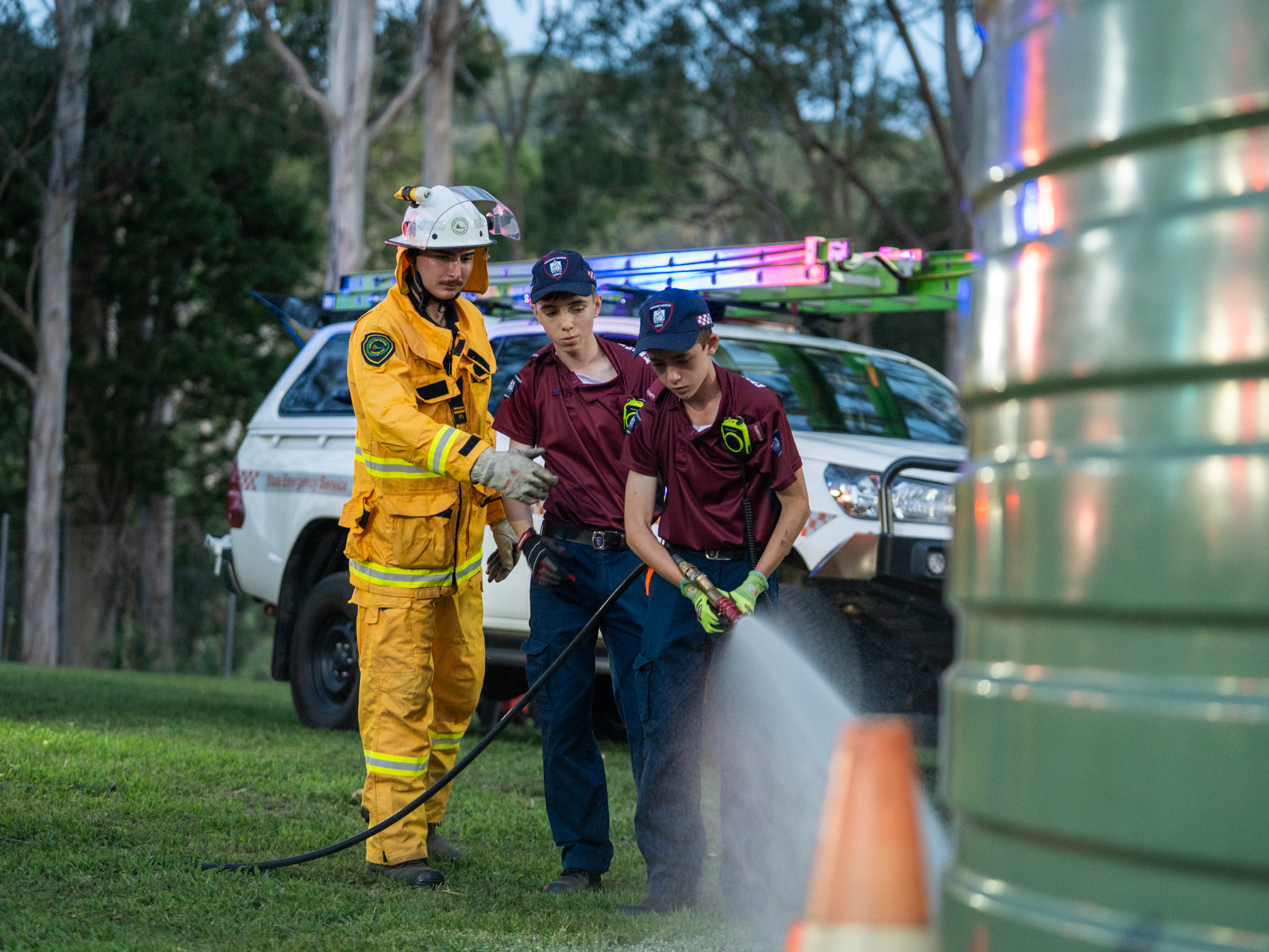 Emergency services cadets and firefighter using a hose
