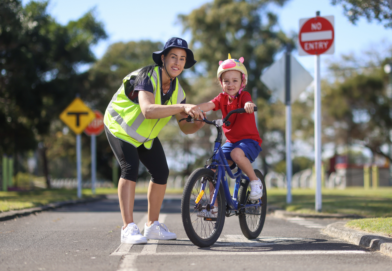 Instructor in visor helping child on bike pretend road, practicing safe riding