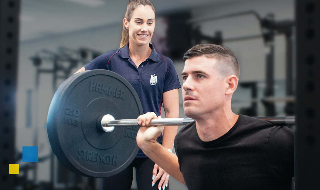 Man holding a barbell while trainer is watching and spotting inside gym