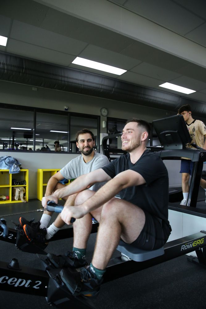 2 gym members smiling at each other on a rower machine