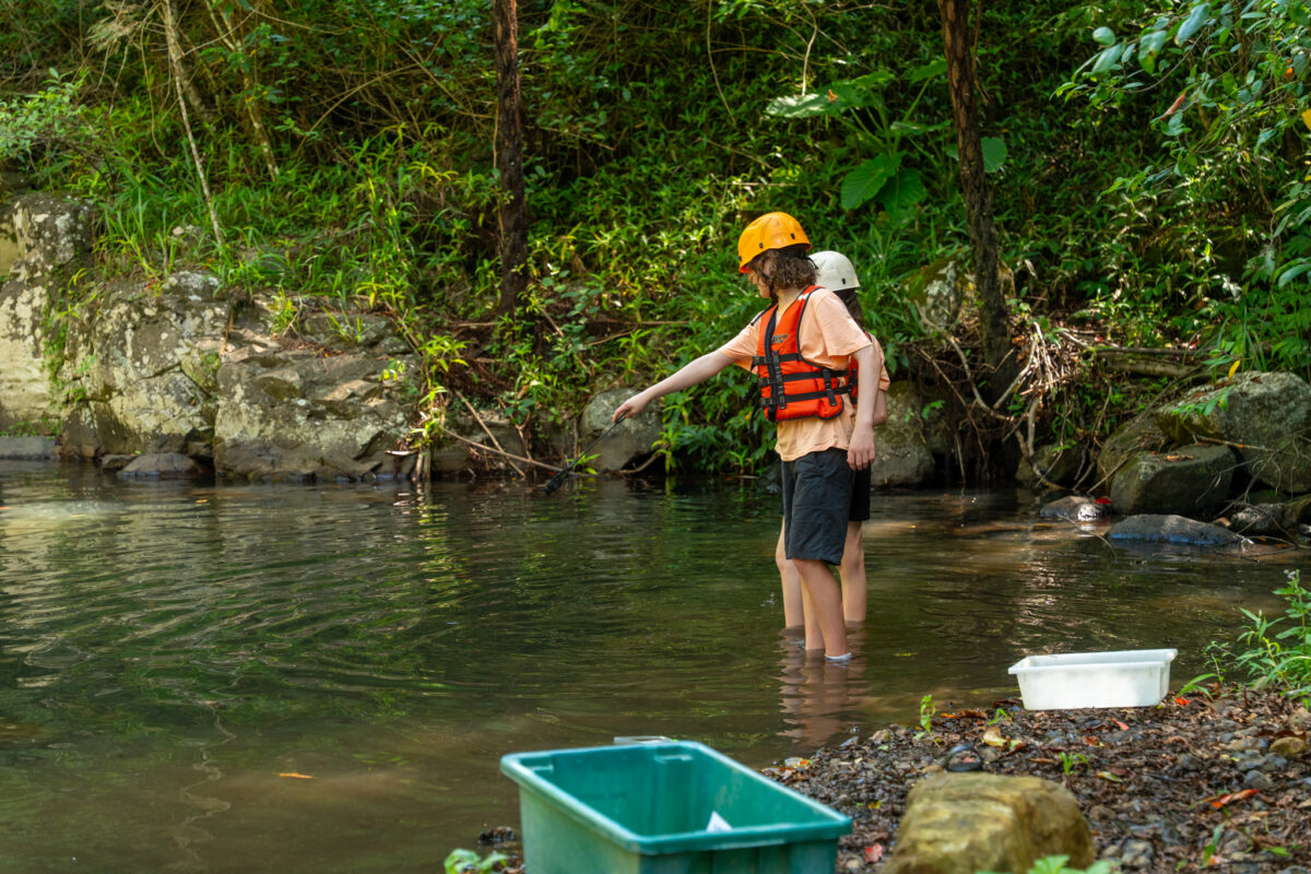 Teens pointing to the river with fishing gear nearby