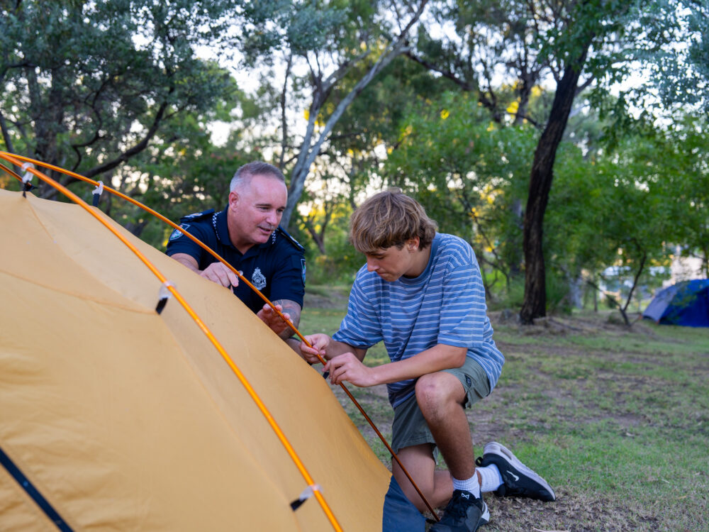 QPS staff member helping teen with setting up their tent